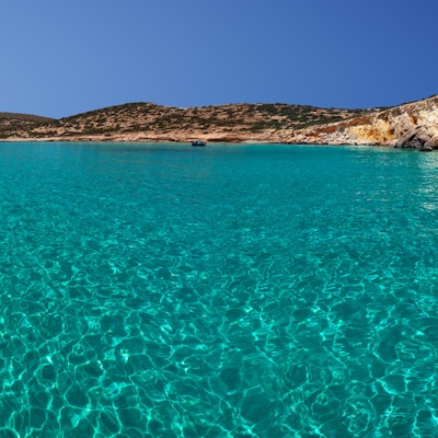 Gjennomsiktig vann og en liten forankret trebåt, på øya Kato Koufonissi, Kykladene, Hellas.