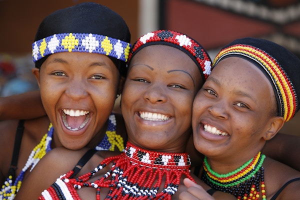 Tre unge Zulu-kvinnevenner, kledd i tradisjonelle zulu-klesplagg, poserer lykkelig for kameraet. Zulu-stammen finnes hovedsakelig i Kwazulu-Natal, Sør-Afrika.
