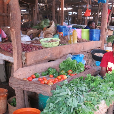 Tre personer sitter og selger grønnsaker på et lokalt marked i Tanzania