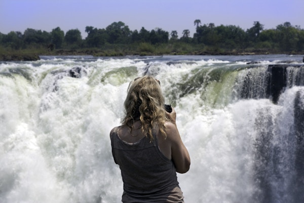 Kvinnelig fotograf som ser på fossene fra Zimbabwe-siden av Zambezi-elven.