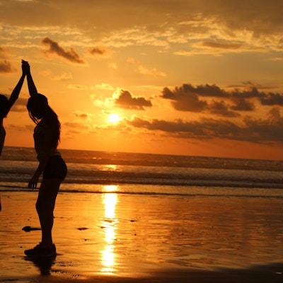 to personer som holder hender på stranden med solnedgangen i bakgrunnen