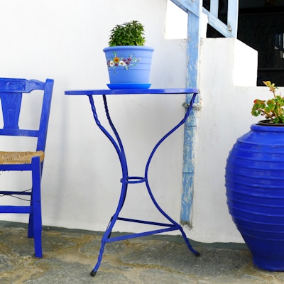 Blå metallstol og bord med en blå blomsterpotte utenfor et hus på den greske øya Milos i Kykladene