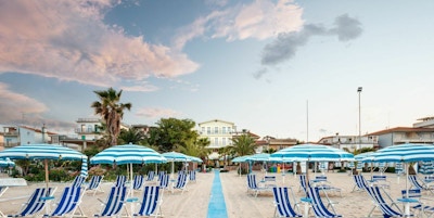 Stranden i San Benedetto del Tronto sett mot veie og bebyggelsen bak stranden men stripete solsenger og parasoller i forgrunnen