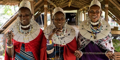 Tre kvinner i lokale drakter og pynt ønsker velkommen til Lake Manyara Kilimamoja