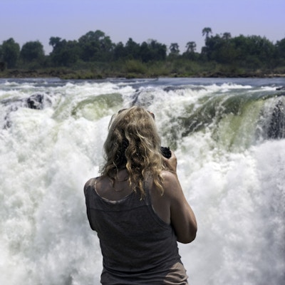 Kvinnelig fotograf som ser på fossene fra Zimbabwe-siden av Zambezi-elven.