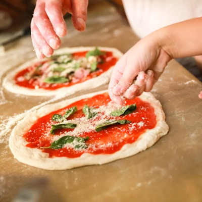 Forbereder klassisk pizza Margherita. Kokker tilsett revet parmesanost. Selektivt fokus
