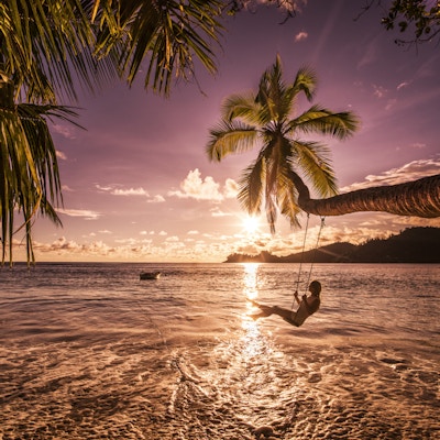 Ung, glad kvinne som gleder seg i en vakker solnedgang på stranden mens hun svinger over vannet.