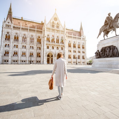 Kvinne som går på plassen nær den berømte parlamentsbygningen under mornignlyset i Budapest, Ungarn