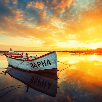Fiskebåt på Varna innsjø med refleksjon i vannet ved solnedgang.