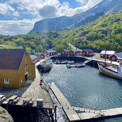 Solen skinner over havnen i Nusfjord med røde og gule hus og to fiskebåter som ligger til havn