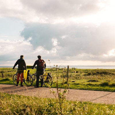 To syklister står og ser på utsikten mot havet ved et gjerde