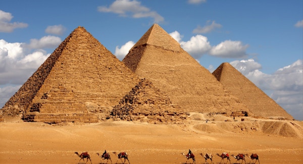 Pyramidene fotografert på avstand med en rekke kameler foran.