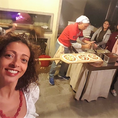 Kvinne tar selfie mot folk som lager pizza