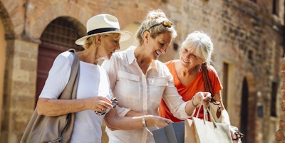 En kvinne står i en gammel del av byen i Italia og holder på med handleposer. Hun viser de to vennene sine hva hun har kjøpt. Alle tre smiler mens de står side om side