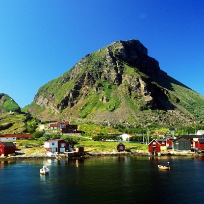 Øya Lovund på Helgelandskysten med røde hus og fjell i bakgrunnen og båter på sjøen