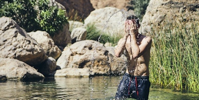 Ung mann spruter vann i ansiktet. Forfriskende i Wadi Shab, Sultanatet i Oman.