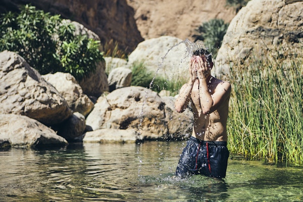 Ung mann spruter vann i ansiktet. Forfriskende i Wadi Shab, Sultanatet i Oman.