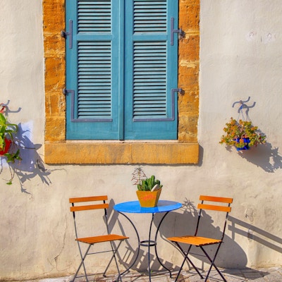Blå skoddervindu og vakre små stoler og et bord på fortauet på Kypros