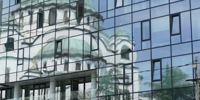 Et bygg i speilglass viser speilbildet til den store, hvite, ortodokse kirken like ved