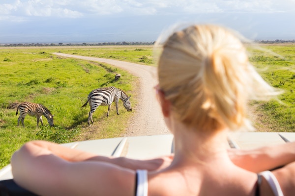 Kvinne på afrikansk villmarkssafari som observerer sebraer fra en safarijeep med åpent tak.