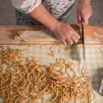 En kokk kutter tacconipasta i strimler med kniv sett ovenfra
