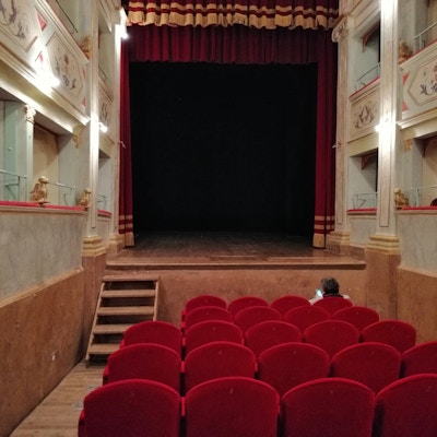 Salen innvendig i Apollo historieske teater i Mondavio, med røde stoler med fem seter i bredden og rødt sceneteppe på den lille scenen