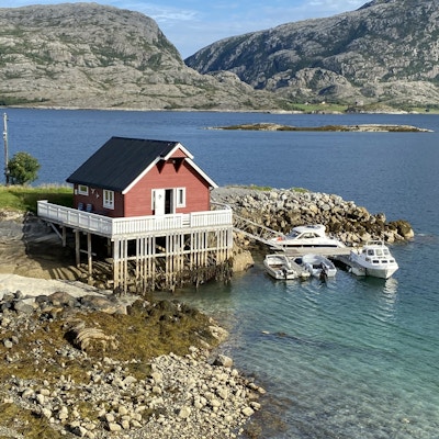 Rød hytte bygget på påler over vannet med båter rundt nede i vannkanten