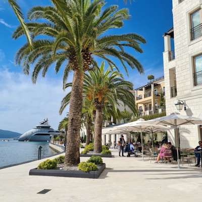 Strandpromenade med palmer og et stor yacht i bakgrunnen