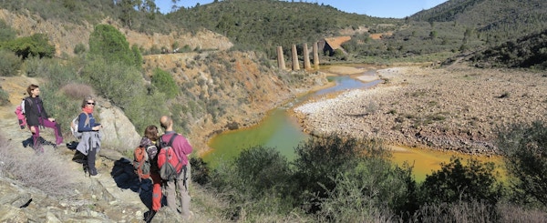 En liten elv farget av mineraler der fire mennesker står og ser utover