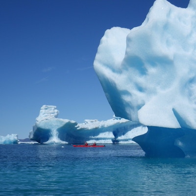 Store isfjell og padlere i røde kajakker i havet utenfor Grønland