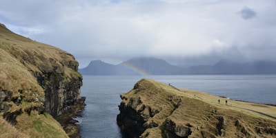 En kløft deler landskapet ved kysten i to og regnet skaper en regnbue over havet