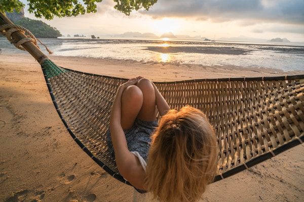 Ung kvinne på en tropisk hage i Thailand som ligger på en hengekøye som slapper av. Solnedgangstid på øya.