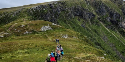 En gruppe mennesker går på sti mot toppen av fjellet i åpent landskap