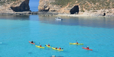 En gruppe padlere padler på knall turkist hav i den blå lagune med steinformasjoner i bakgrunnen