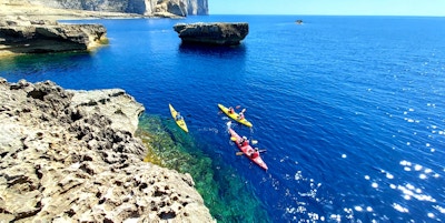 Fem kajakkpadlere padler langs kalksteinslandskapet utenfor Gozo