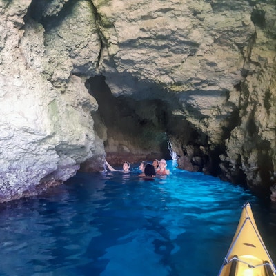 en gruppe mennesker bader i en grotte med knall blått hav