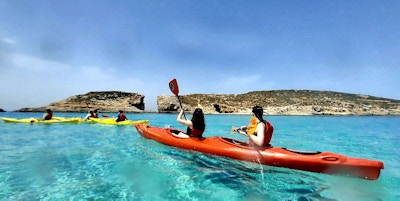 En gruppe kajakkpadlere padler i turkist hav utenfor Gozo