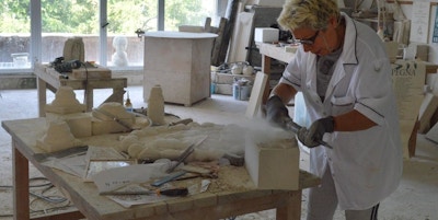 En dame bruker verktøy i sitt verksted og jobber med sandstein for å lage statuer