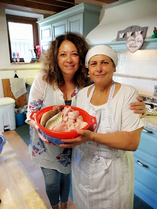 Kokken Ivana holder en bolle med rå fisk og poserer for bildet sammen med en italiensk dame på et kjøkken med lyseblå skapdører