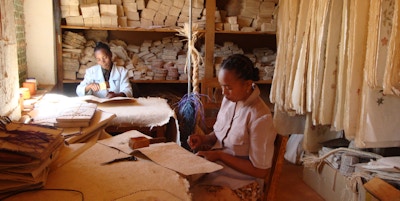 To kvinner sitter og tegner og skriver på tykt papir laget av bark