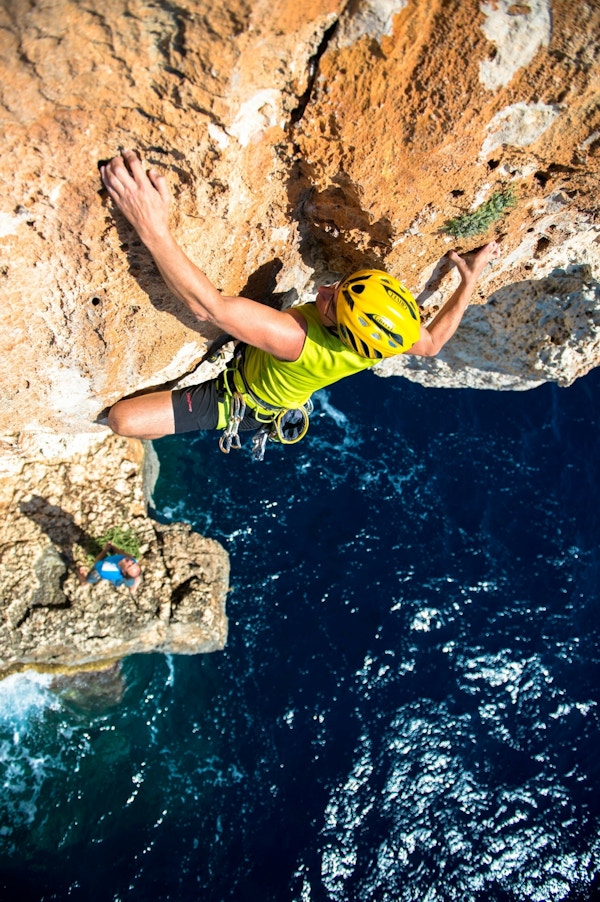 En klatrer sett ovenfra som klatrer oppover fjellveggen over havet