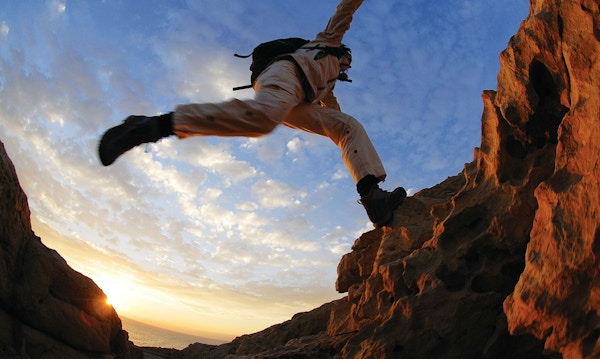 En vandrer hopper fra en stein til en annen, med solnedgangen i bakgrunnen