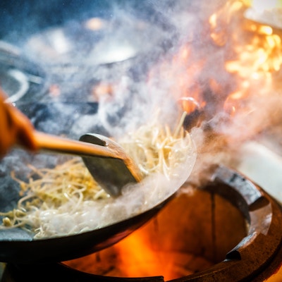 Kokk i restaurantkjøkken ved komfyren med høye brennende flammer