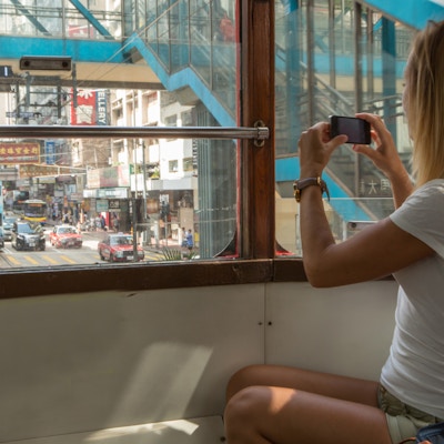 Ung kvinne på en trikk i Hong Kong tar bilder av de travle gatene ved hjelp av en mobiltelefon.