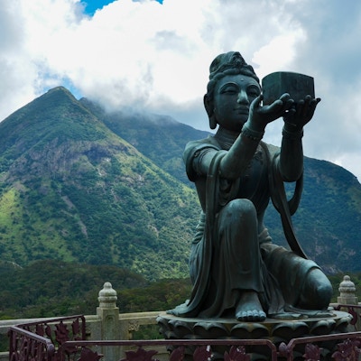 Grønne områder med fjell og en Buddha i forgrunnen