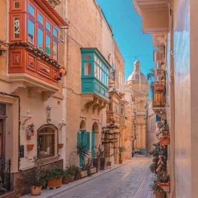 En gate i Birgu, Malta, med typiske maltesiske balkonger malt i flotte farger og domen på kirken i enden av gaten