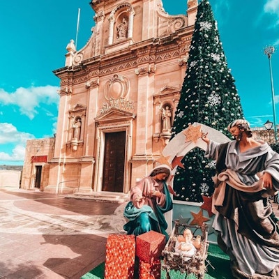 Julekrybbe med statuer av Josef, Maria og Jesusbarnet foran et juletre utenfor en kirke på Malta