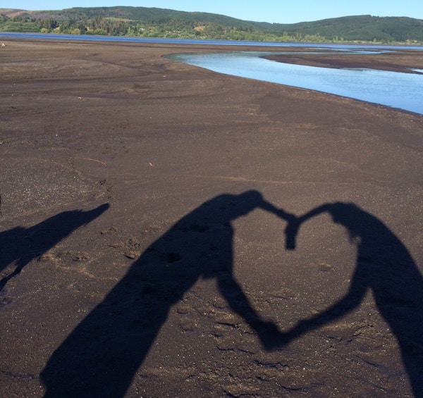 Strand med mørk sand der to mennesker lager en skygge formet som et hjerte