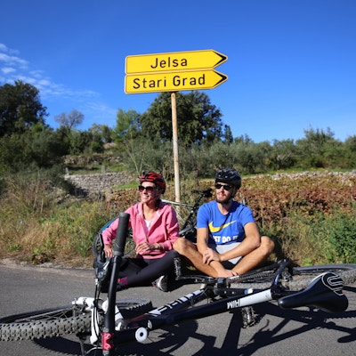 To personer sitter og slapper av på siden av en vei med sykkelen lagt i bakken