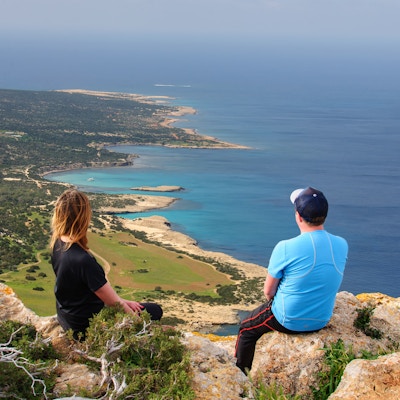 To personer sitter og ser utover havet på en høyde